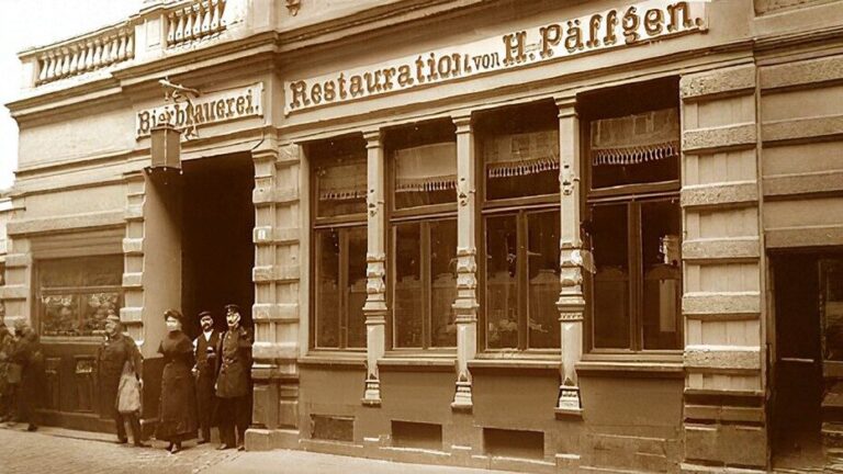 Sepia-Foto von Menschen, die vor einem historischen deutschen Restaurant und einer Brauerei mit den Schildern "Bierbrauerei" und "Restauration von H. Pfaffen" stehen. Das Gebäude ist mit großen Fenstern und kunstvollem Mauerwerk ausgestattet.